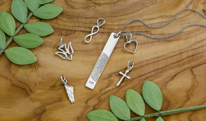 sterling silver vertical bar pendant engraved with a fingerprint beside sterling silver symbolic jewelry charms