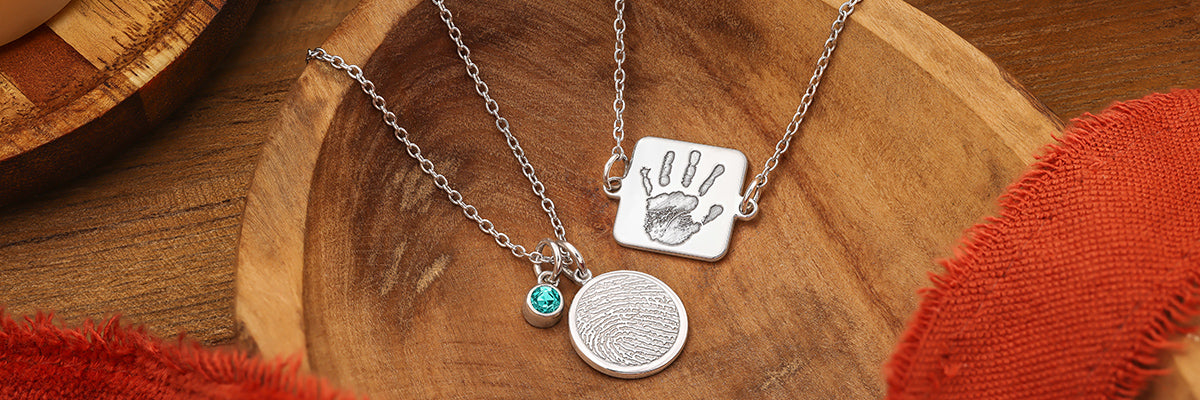 silver charms on a necklace and bracelet featuring a fingerprint and handprint