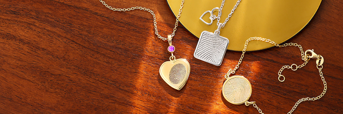 silver charms on a necklace and bracelet featuring a fingerprint and handprint