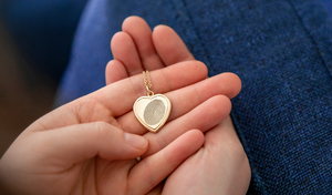 person holding a yellow gold heart pendant engraved with a fingerprint