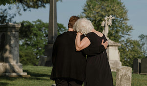 two grieving friends comforting each other at a cemetary