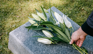 person laying white flowers on a grave during a funeral