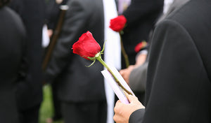 person in black holding a red rose and program at a funeral service