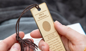 person holding an engraved brass bookmark with fingerprint and inscription