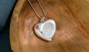 sterling silver urn pendant necklace that holds ashes with a pink swarovksi birthstone closure and an engraved fingerprint on the front