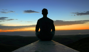 person meditating in front of a sunrise